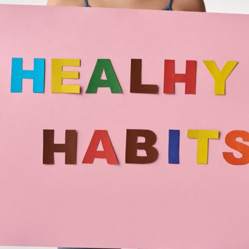 A woman holds a pink poster with colorful letters spelling 'HEALTHY HABITS'.