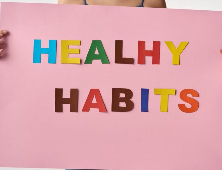 A woman holds a pink poster with colorful letters spelling 'HEALTHY HABITS'.